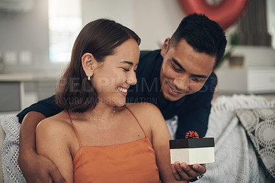 Buy stock photo Love, surprise and man giving his wife a gift for valentines day, anniversary or romantic event. Happy, smile and husband giving his woman a present while relaxing on the sofa in living room at home.