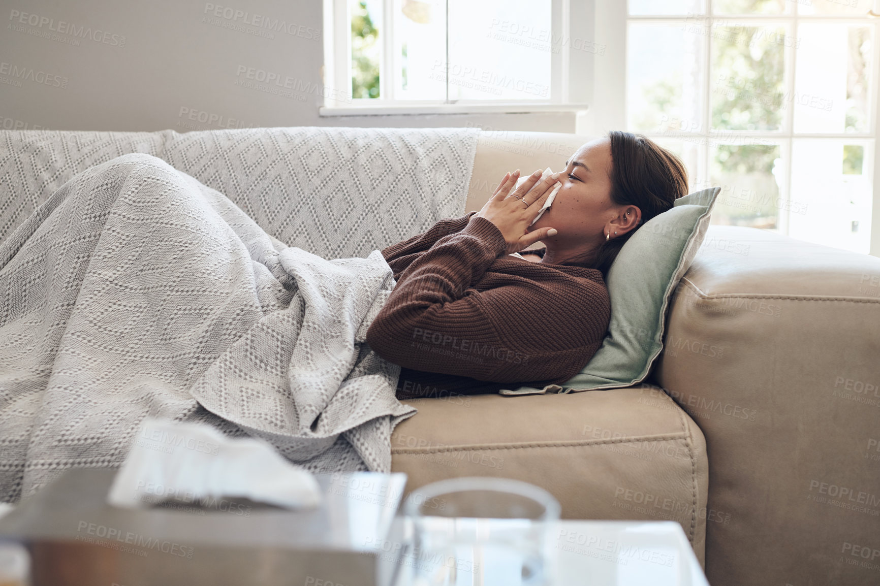 Buy stock photo Sick woman, sneeze and blowing nose with flu, cold or illness on living room sofa at home. Young female person with tissue for bacteria, fever or influenza in fatigue or rest on lounge couch at house