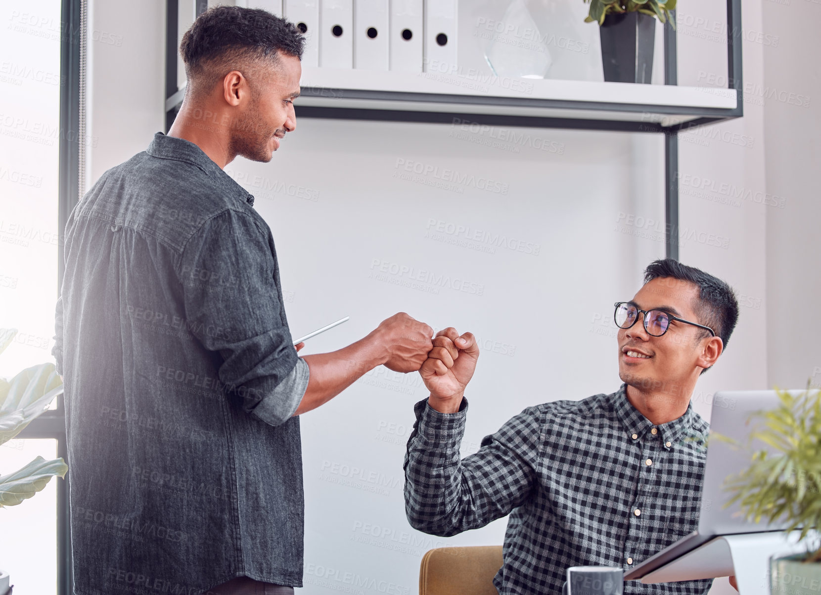 Buy stock photo Shot of two young businessman giving each other a fist bump in an office