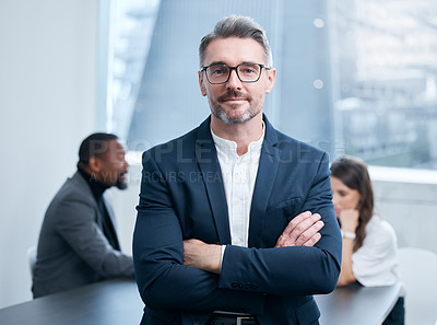 Buy stock photo Portrait of a confident mature businessman standing in an office with his colleagues in the background