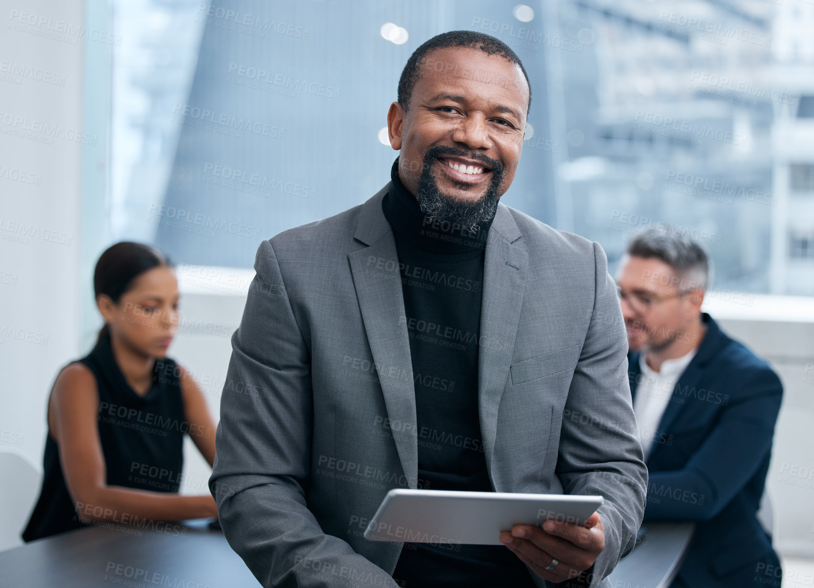 Buy stock photo Portrait of a mature businessman using a digital tablet in an office with his colleagues in the background