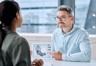 Buy stock photo Shot of a mature businessman speaking to a colleague while analysing graphs on a digital tablet in an office