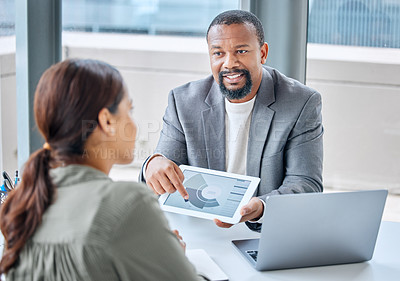 Buy stock photo Shot of a mature businessman speaking to a colleague while analysing graphs on a digital tablet in an office