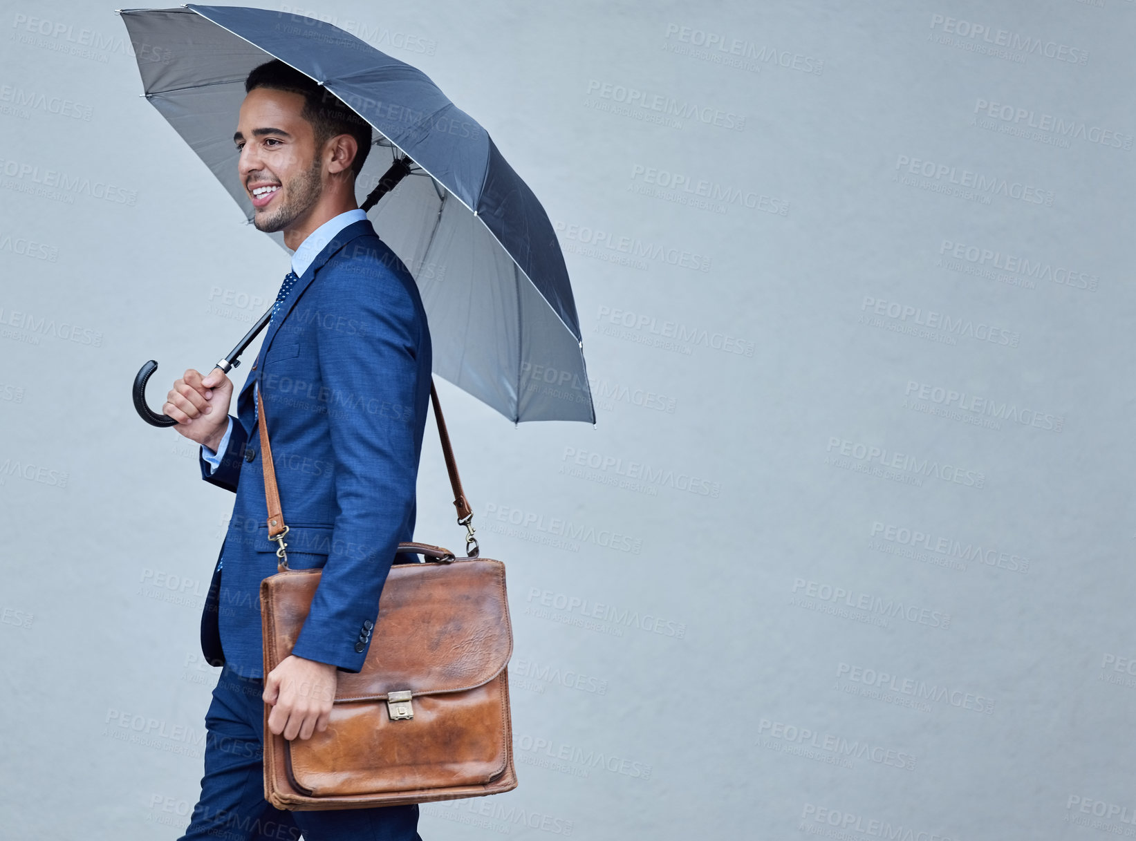 Buy stock photo Cropped shot of a handsome young businessman posing in studio with his satchel and umbrella against a grey background