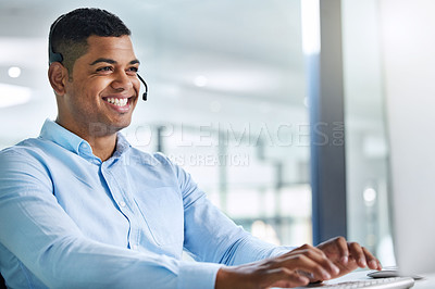 Buy stock photo Shot of a handsome young call centre agent sitting in the office and wearing a headset while using his computer