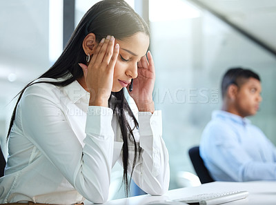 Buy stock photo Shot of a young call centre agent sitting in the office and suffering from a headache while wearing a headset