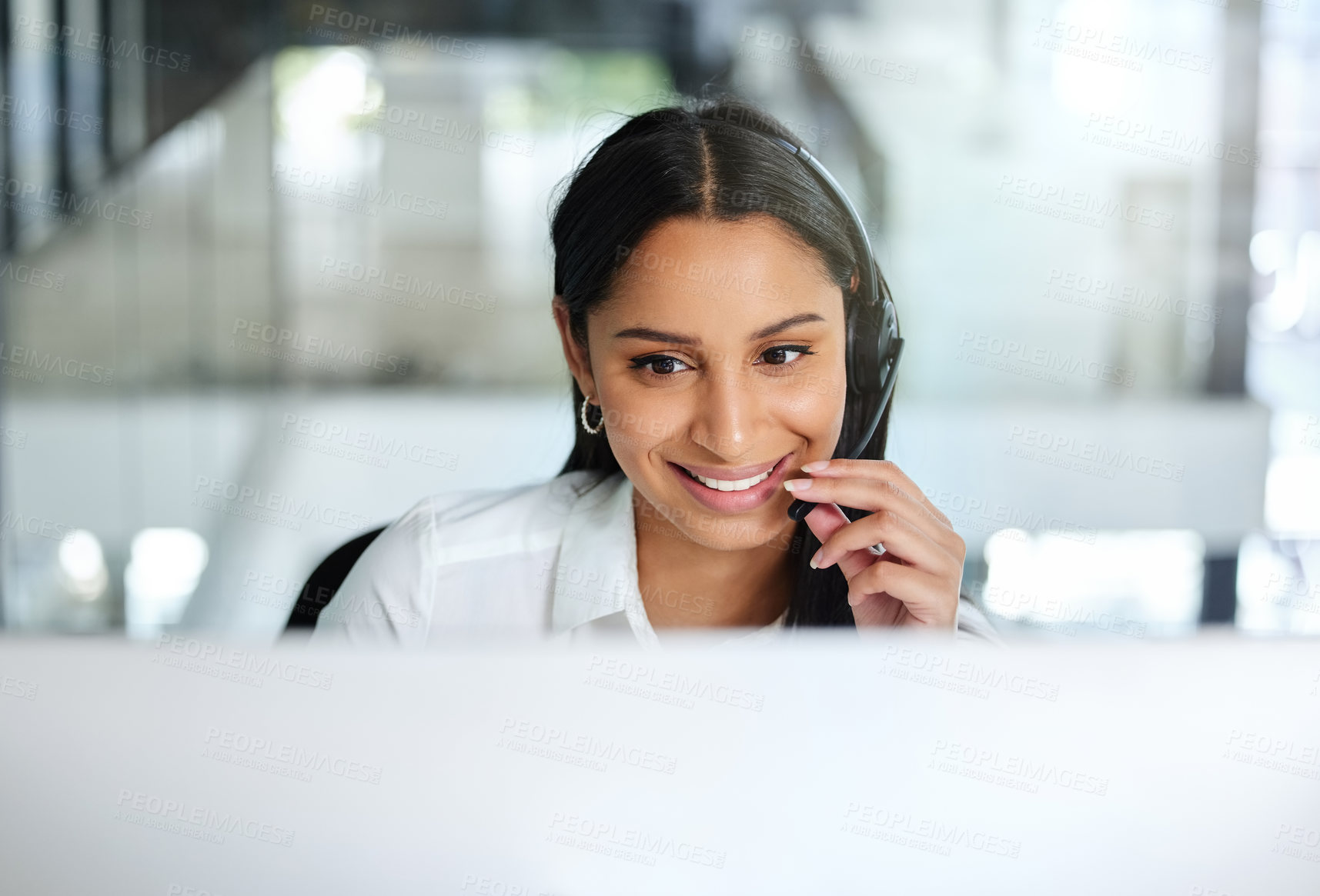 Buy stock photo Shot of an attractive young call centre agent sitting in the office and wearing a headset while using her computer