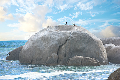 Buy stock photo Scenic view of a beach with rocks or boulders and sea water. The landscape of a rocky coastline in spring. A big rock in the middle of the ocean with birds on it and blue sky background in summer. 