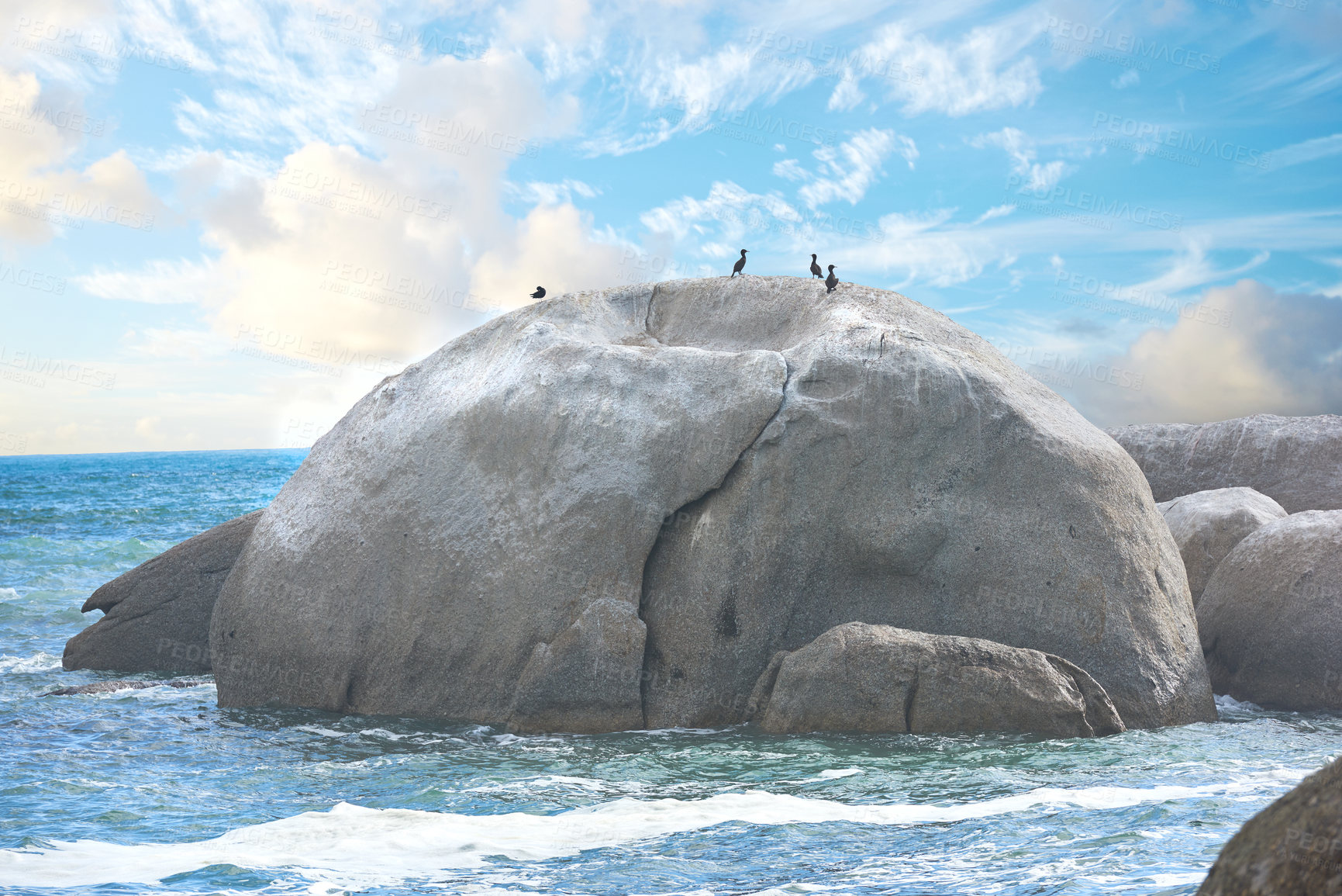 Buy stock photo Scenic view of a beach with rocks or boulders and sea water. The landscape of a rocky coastline in spring. A big rock in the middle of the ocean with birds on it and blue sky background in summer. 