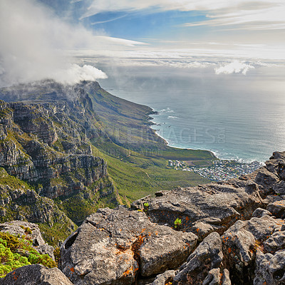 Buy stock photo Aerial view of a majestic mountain landscape, an ocean and a city in a valley during a cloudy day. Beautiful scenery of a cloudscaped sky above a rocky terrain with the sea below with copy space