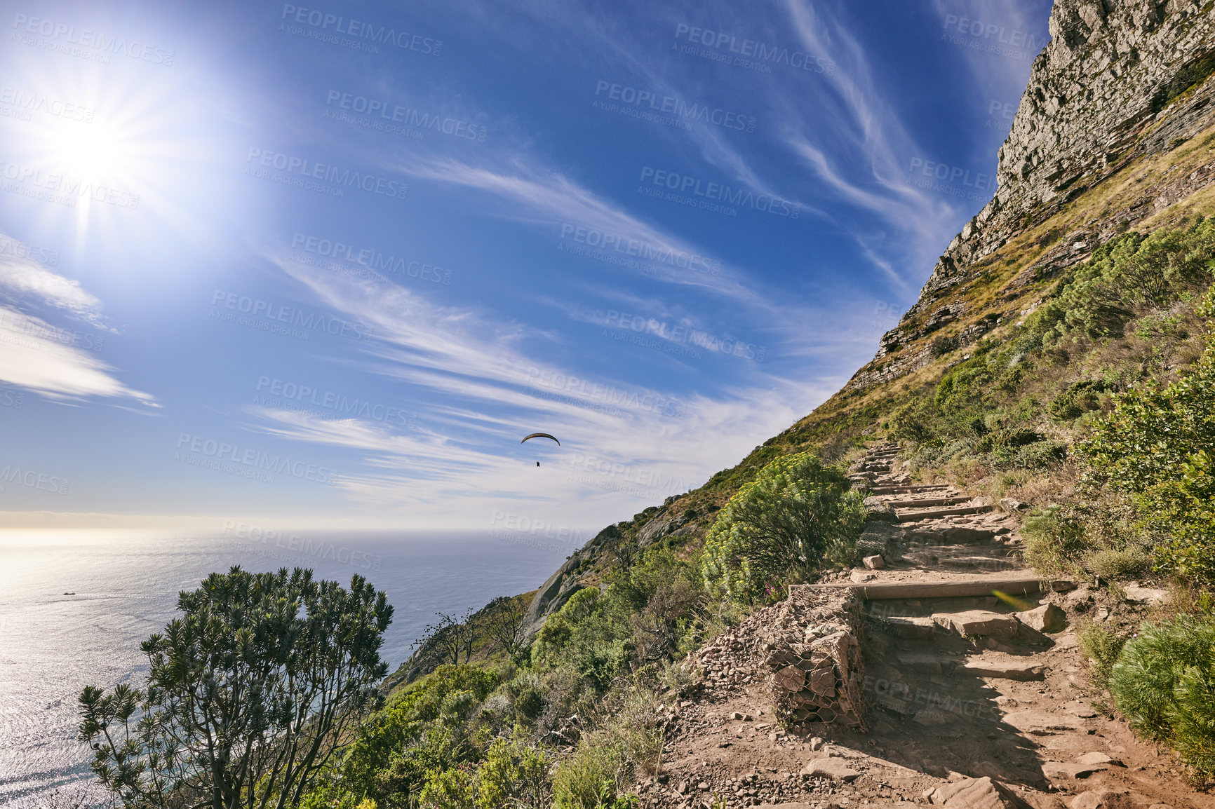 Buy stock photo A hiking trail up a rocky mountain with green plants growing and cloudy blue sky background. The landscape of a path in a beautiful coastal trekking location near the ocean outdoors in nature