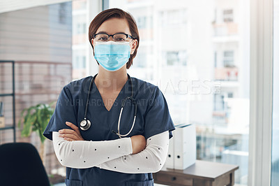 Buy stock photo Shot of a young doctor with her arms crossed while wearing a mask in an office