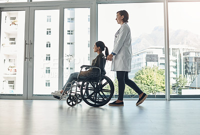 Buy stock photo Shot of a young female doctor pushing a patient in a wheelchair in a hospital