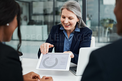 Buy stock photo Shot of a mature businesswoman using a digital tablet during a meeting with colleagues in a modern office