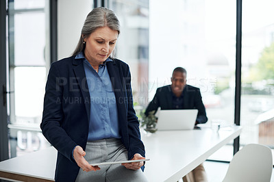 Buy stock photo Shot of a mature businesswoman using a digital tablet during a meeting in a modern office