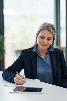 Buy stock photo Shot of a mature businesswoman filling out paperwork at a desk in a modern office