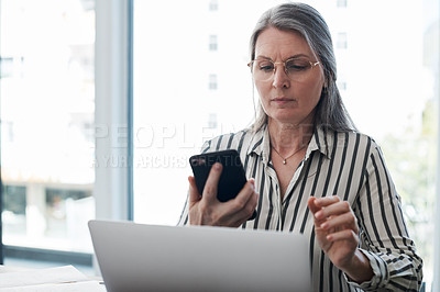 Buy stock photo Shot of a mature businesswoman using her smartphone and laptop in a modern office