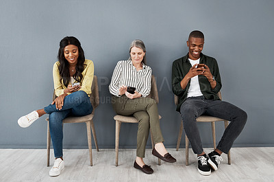 Buy stock photo Shot of a diverse group of people taking a break from a busy day by scrolling social media against a grey wall