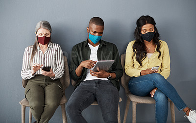 Buy stock photo Shot of a cautious group of people socially distancing while using their smart devices against a grey wall