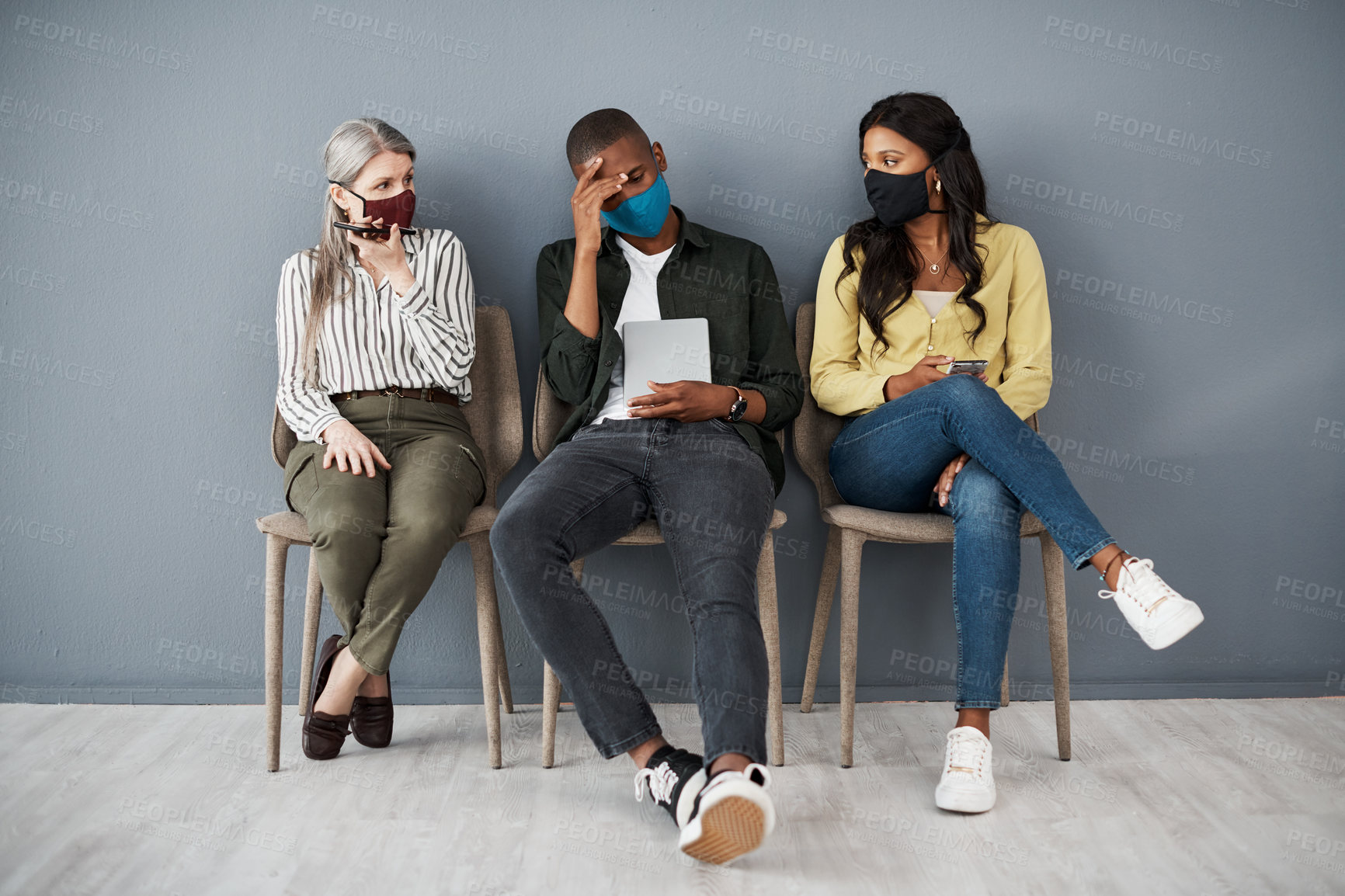 Buy stock photo Shot of an accused young man looking guilty between two woman behind face masks against a grey wall