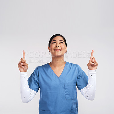 Buy stock photo Shot of a young doctor wearing scrubs pointing up against a white background