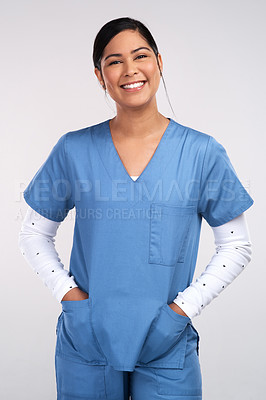 Buy stock photo Portrait of a young doctor standing with her hands tucked into her scrubs against a white background