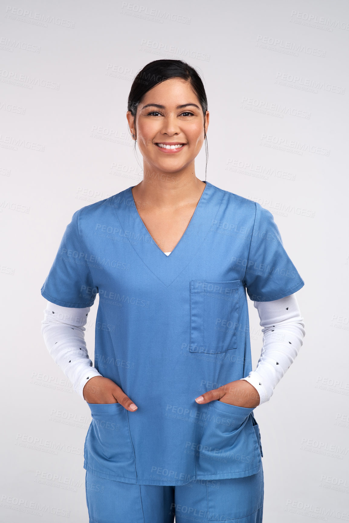 Buy stock photo Portrait of a young doctor standing with her hands tucked into her scrubs against a white background