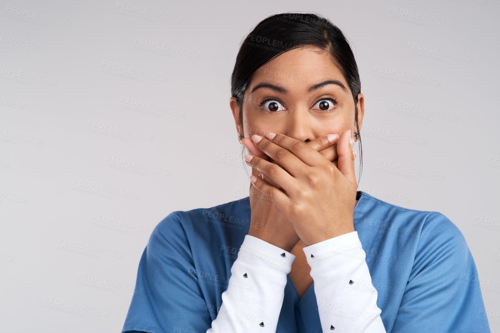Buy stock photo Portrait of a shocked young doctor covering her mouth in scrubs against a white background