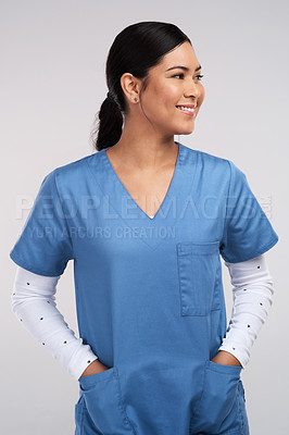 Buy stock photo Shot of a young doctor standing with her hands tucked into her scrubs against a white background