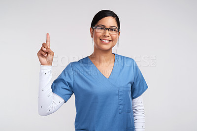 Buy stock photo Portrait of a young doctor wearing glasses and scrubs, pointing up against a white background