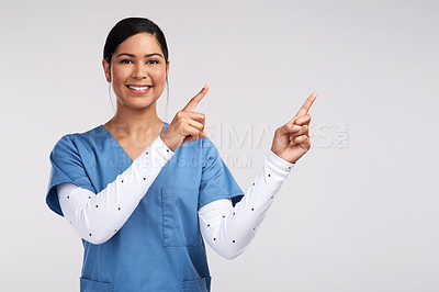 Buy stock photo Portrait of a young doctor wearing scrubs and pointing to her left against a white background