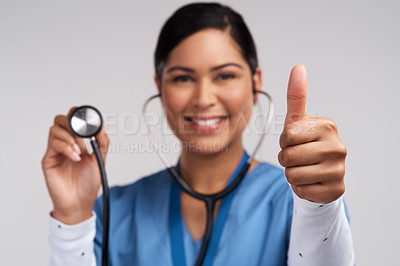 Buy stock photo Portrait of a young doctor showing thumbs up and holding a stethoscope against a white background