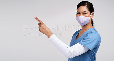 Buy stock photo Portrait of a young doctor wearing a surgical face mask and pointing to her right against a white background