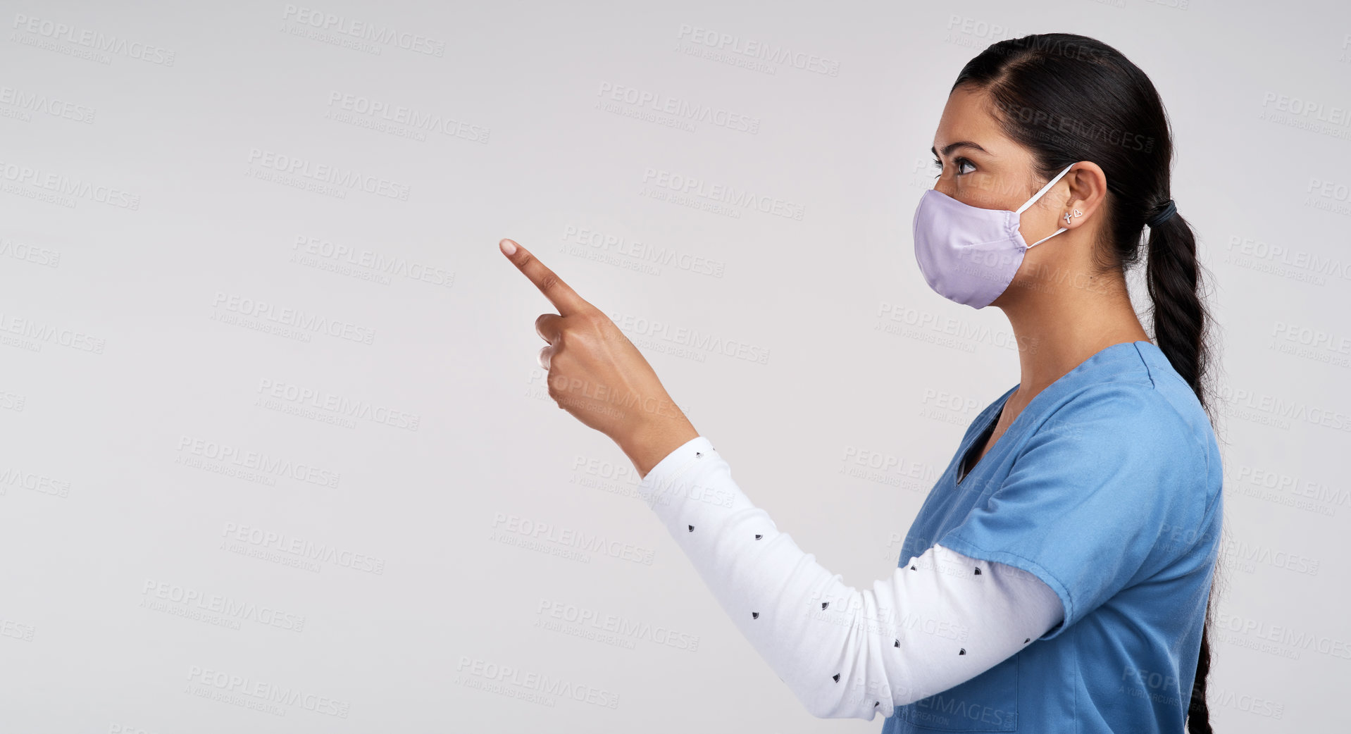 Buy stock photo Side shot of a young doctor wearing a surgical face mask and pointing to her right against a white background