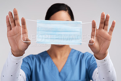 Buy stock photo Portrait of a young doctor holding her surgical face mask up against a white background