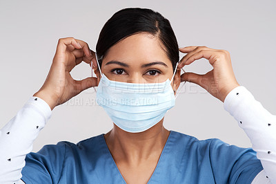 Buy stock photo Portrait of a young doctor adjusting her surgical face mask against a white background