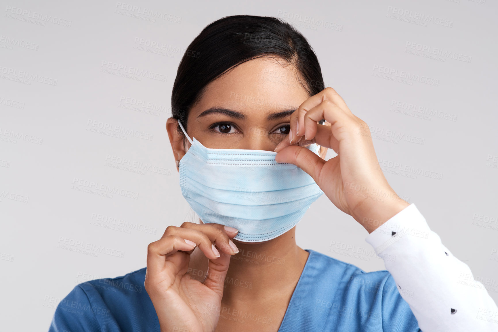 Buy stock photo Portrait of a young doctor adjusting her surgical face mask against a white background