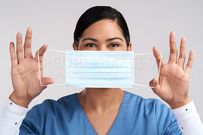 Buy stock photo Portrait of a young doctor holding her surgical face mask up against a white background