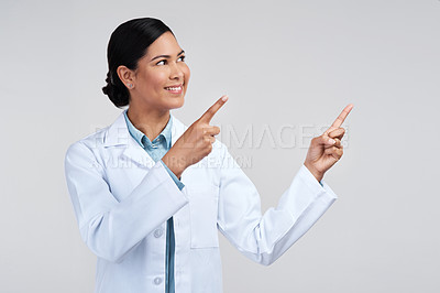 Buy stock photo Cropped shot of an attractive young female scientist pointing towards copyspace in studio against a grey background