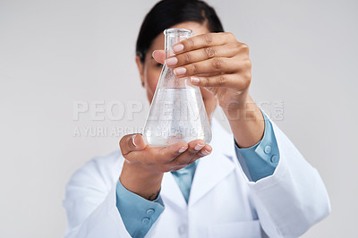 Buy stock photo Cropped shot of an unrecognizable young female scientist examining a beaker filled with liquid in studio against a grey background