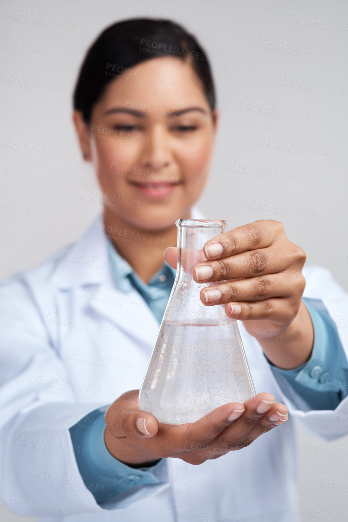 Buy stock photo Cropped shot of an attractive young female scientist examining a beaker filled with liquid in studio against a grey background