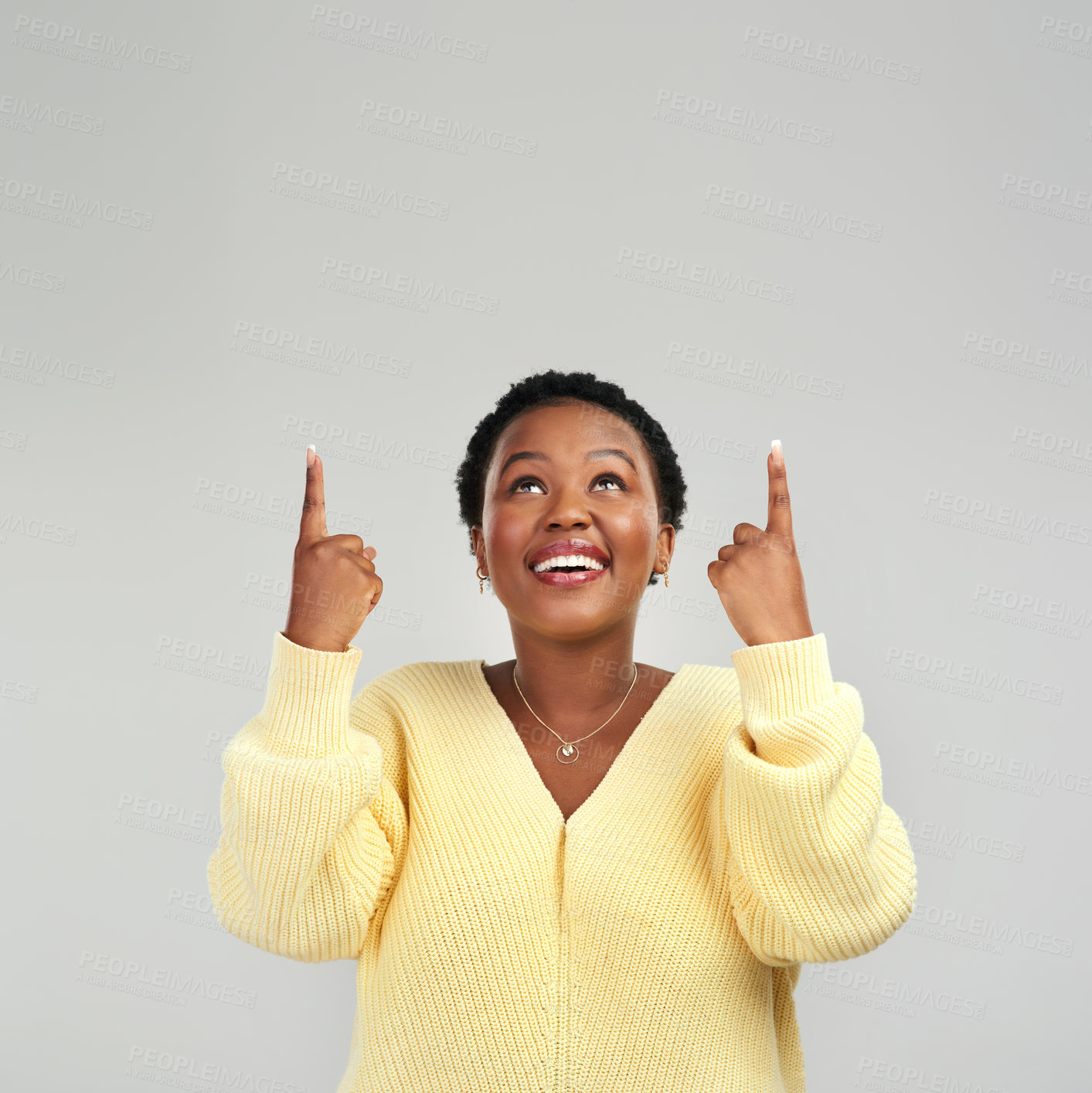 Buy stock photo Shot of a young woman pointing at copy-space while posing against a grey background