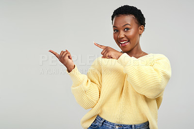 Buy stock photo Shot of a young woman pointing at copy-space while posing against a grey background