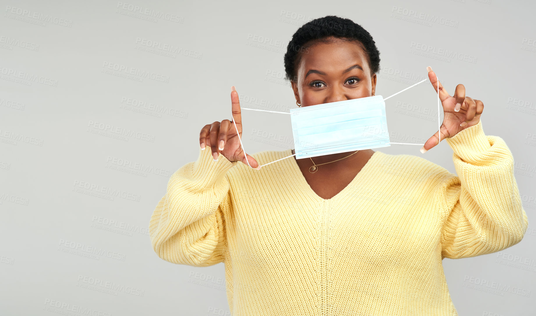 Buy stock photo Shot of a young woman holding up a surgical mask while standing against a grey background