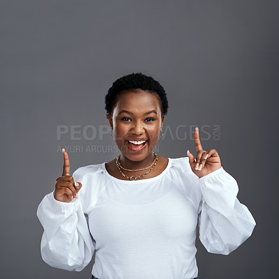 Buy stock photo Shot of a young woman pointing at copy-space while posing against a grey background