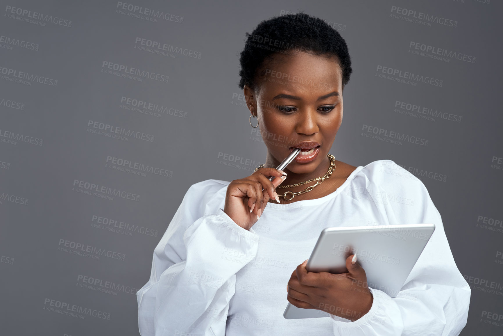 Buy stock photo Shot of a young woman holding a digital tablet while posing against a grey background