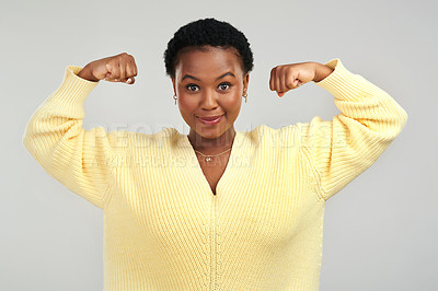 Buy stock photo Shot of a young woman flexing while posing against a grey background