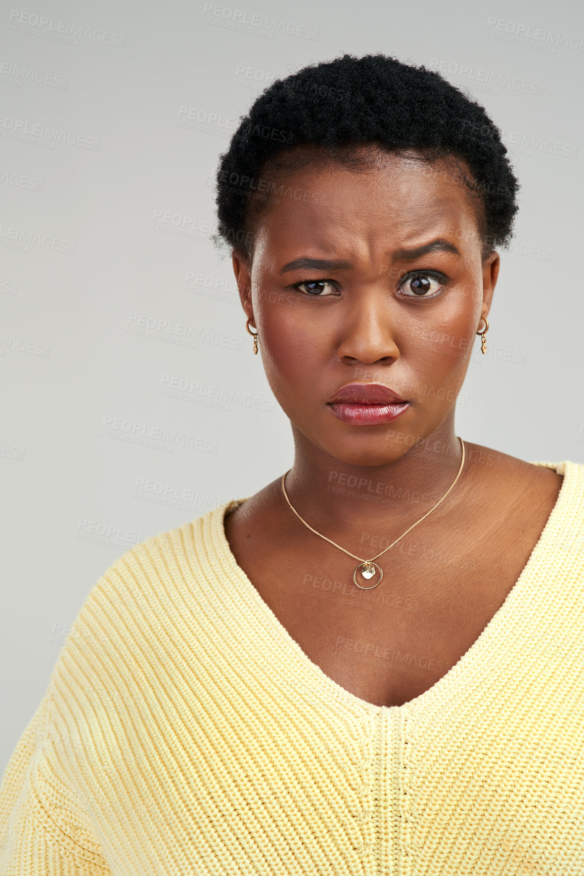 Buy stock photo Shot of a young woman frowning while standing against a grey background