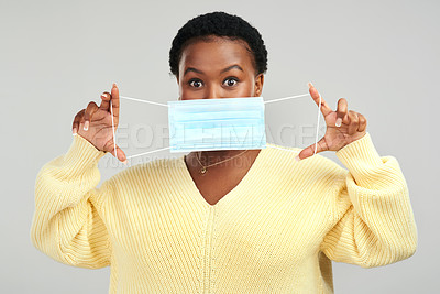 Buy stock photo Shot of a young woman holding up a surgical mask while standing against a grey background