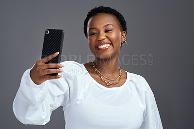 Buy stock photo Shot of a beautiful young woman taking a selfie while posing against a grey background